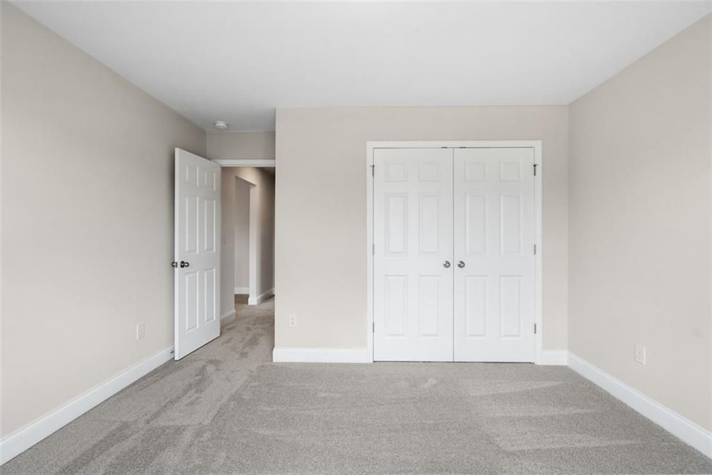 Spacious neutral bedroom with beige walls, white double closet doors, and hallway access in Davidson Homes The Willow B, Hoschton, Georgia