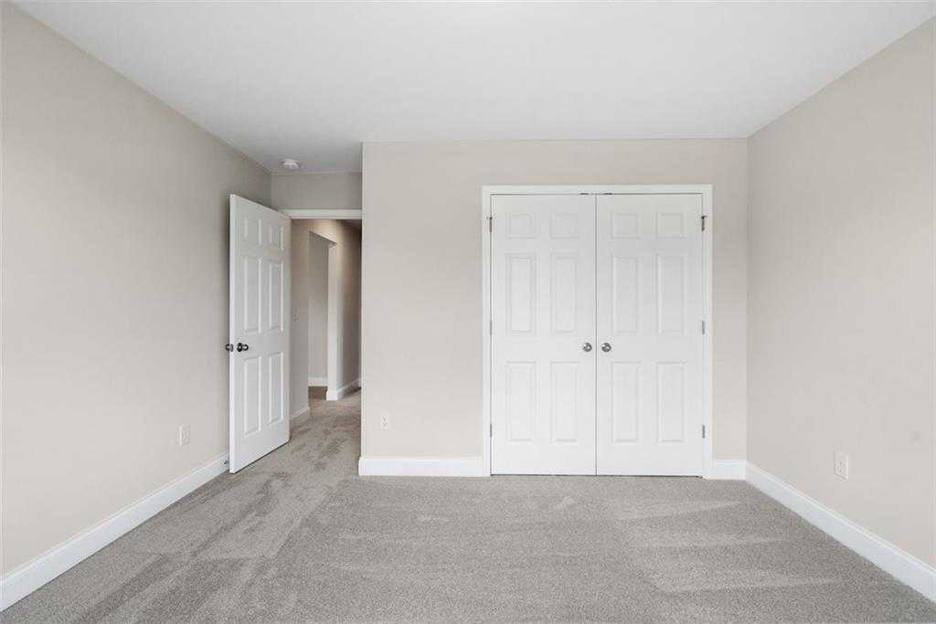 Spacious neutral bedroom with beige walls, white double closet doors, and hallway access in Davidson Homes The Willow B, Hoschton, Georgia