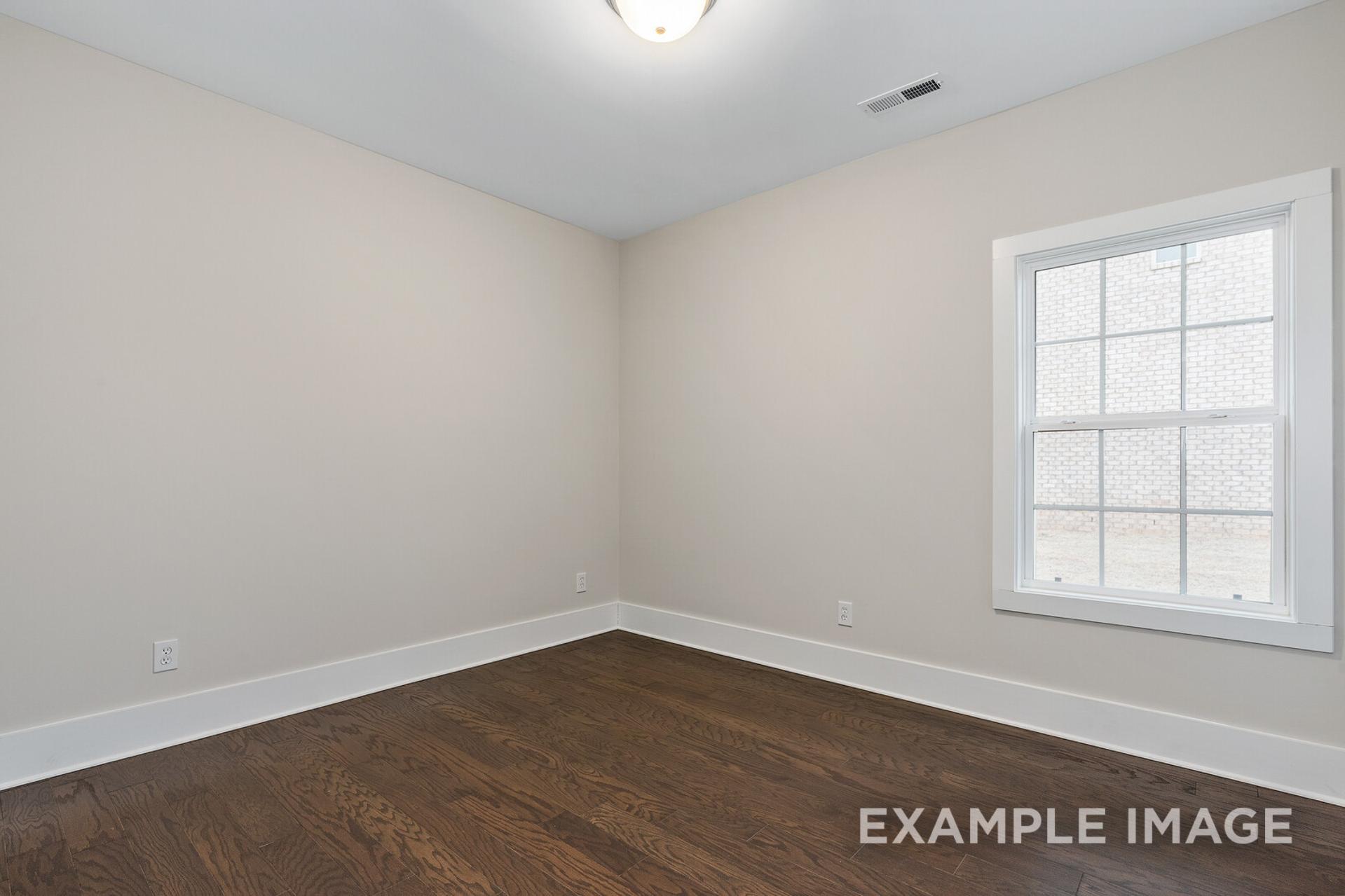 Spacious empty bedroom in The Rockford floor plan with beige walls, oak hardwood floors, and large grid window