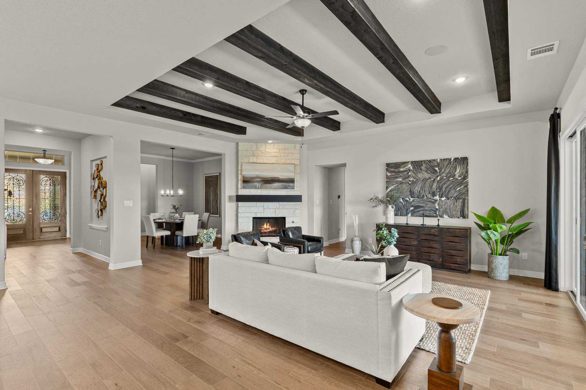 Open-concept living room in The Summerlin B featuring vaulted beamed ceiling, white sectional sofa, stone fireplace, and dining area