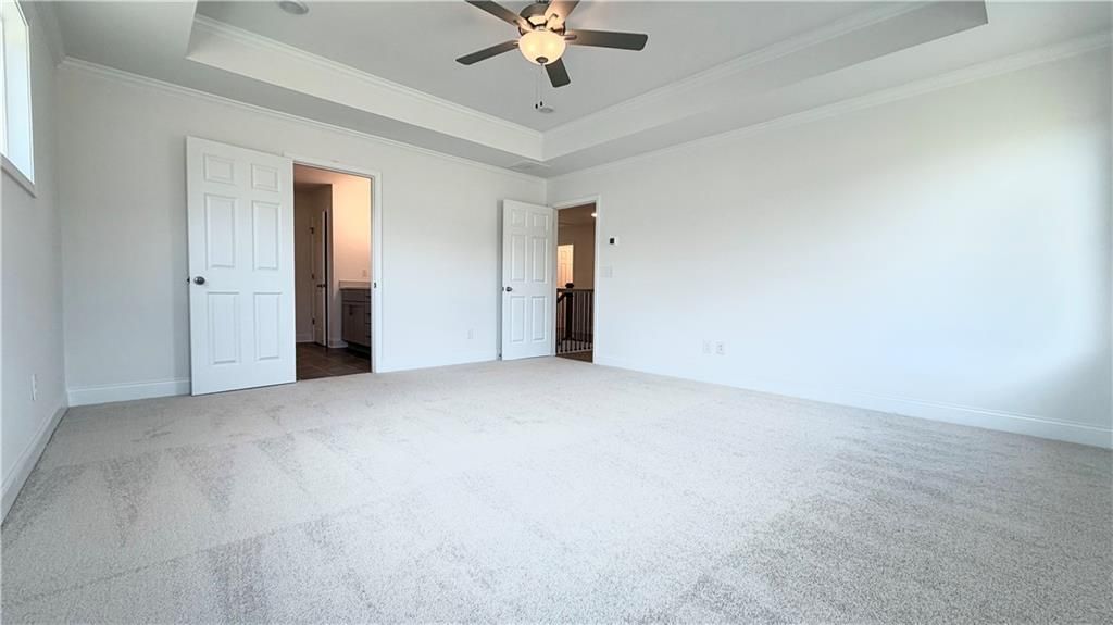 Spacious primary bedroom with tray ceiling and plush carpet in The Hickory C floor plan, Wehunt Meadows, Hoschton.