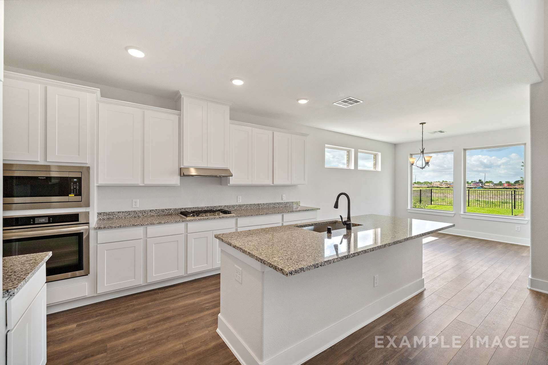 Bright open-concept kitchen in The Victoria by Davidson Homes with granite island, white cabinetry, and hardwood-style flooring