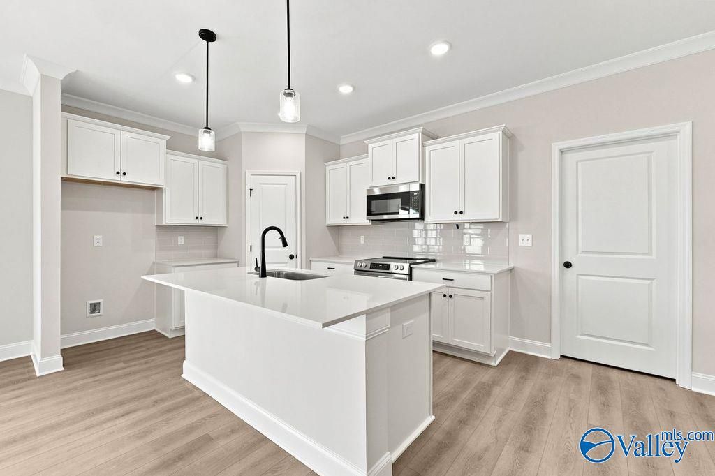 Modern kitchen with white cabinets, quartz island, and pendant lighting in The Camilla B floor plan, Hartselle, Alabama.