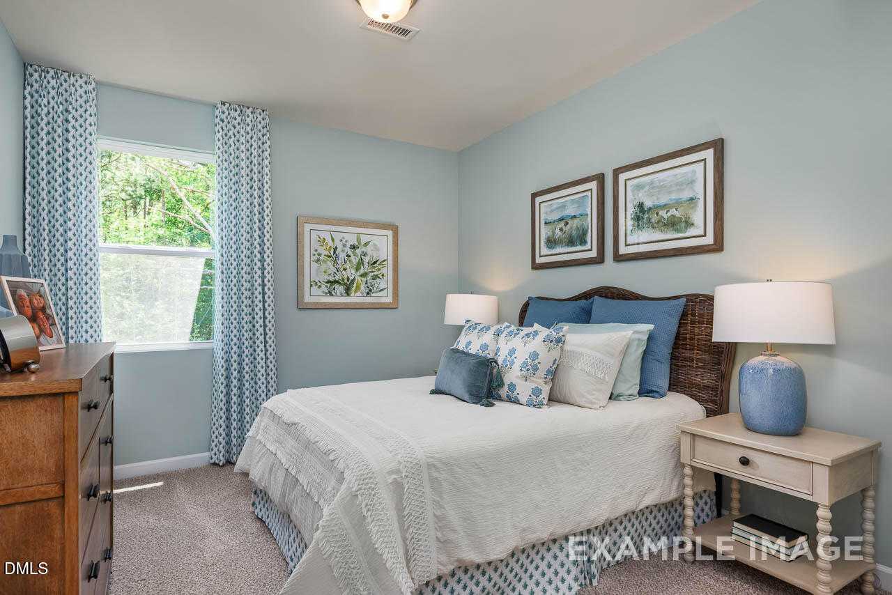 Cozy blue bedroom with rattan headboard bed, pillows, lamps, and floral art in Davidson Homes The Willow B, Lillington, NC