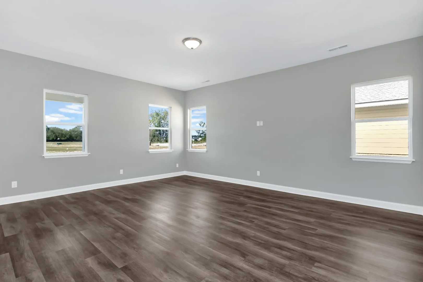 Spacious empty living room in The Arcadia M home with gray walls, hardwood floors, large windows overlooking greenery