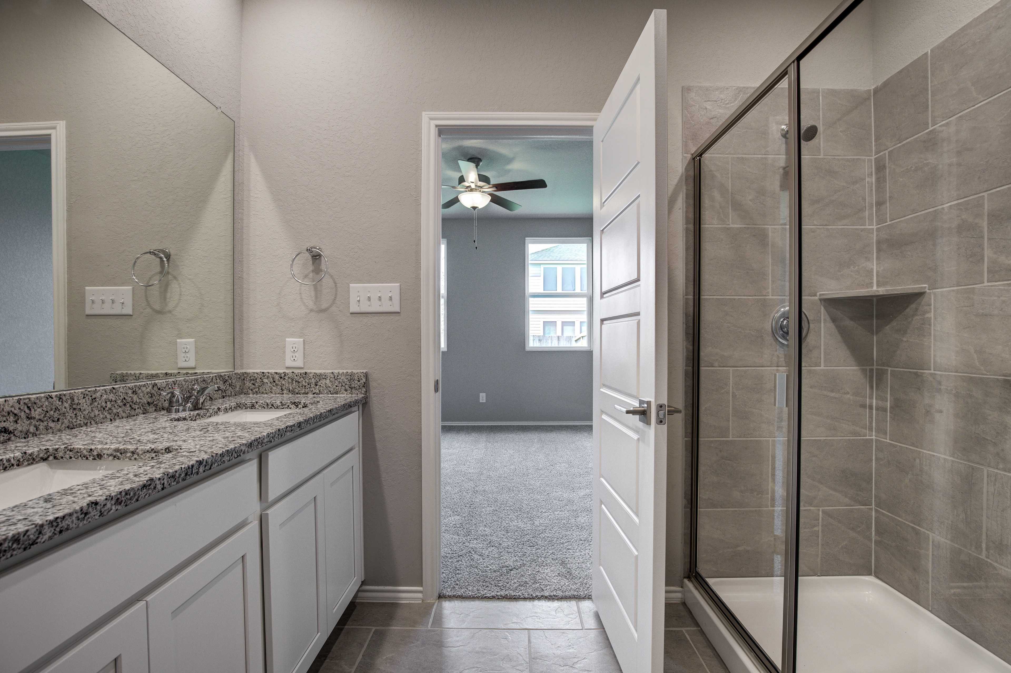 Spacious master bathroom in The Asheville with double granite vanity, white cabinets, and frameless glass walk-in shower