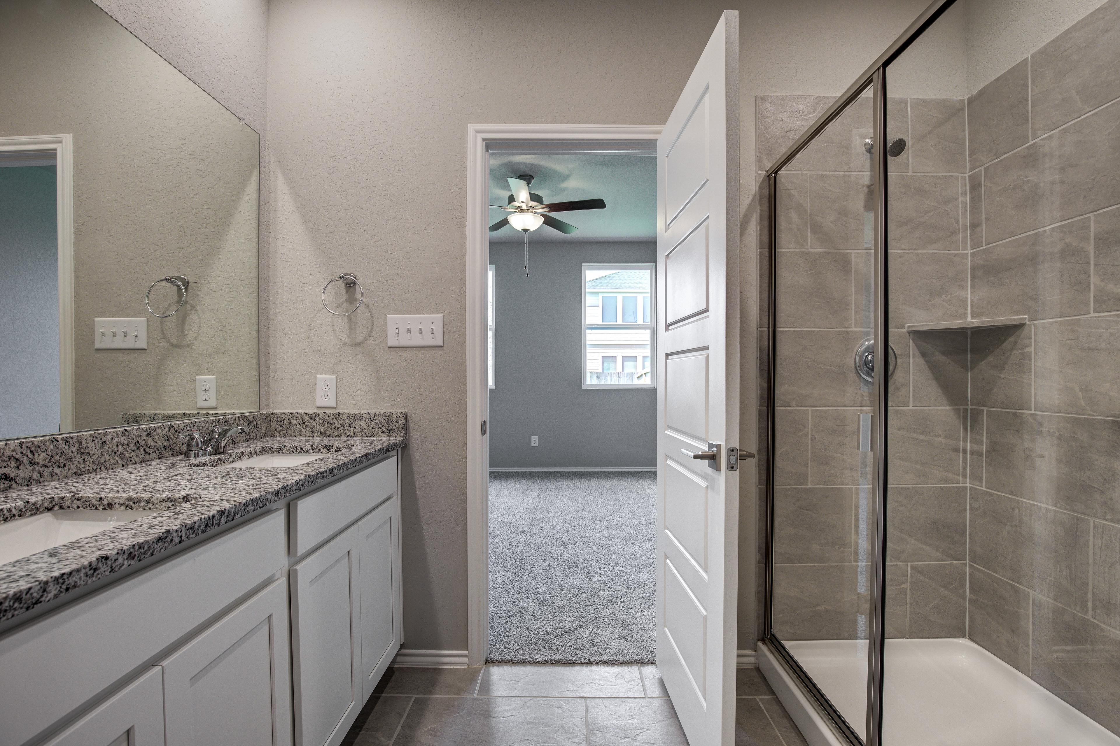 Spacious master bathroom in The Asheville featuring double granite vanity, large mirrors, and tiled walk-in shower