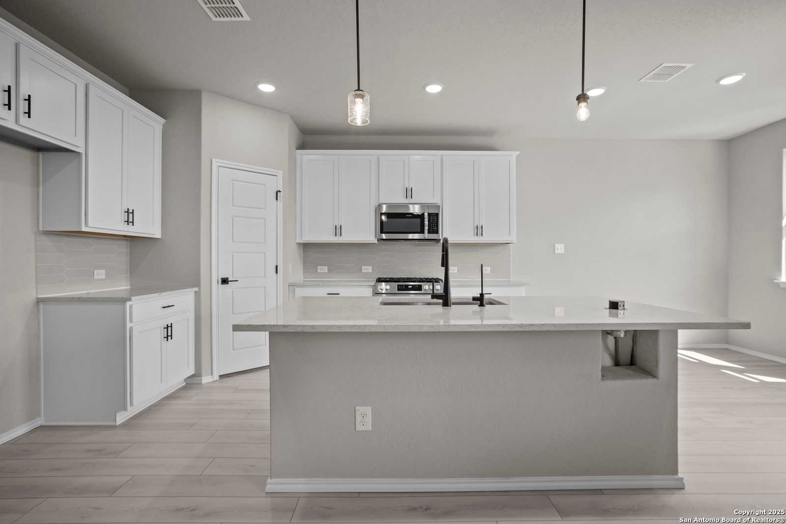 Bright kitchen with white cabinets, quartz island sink, stainless appliances in The Asheville E by Davidson Homes, Converse, Texas