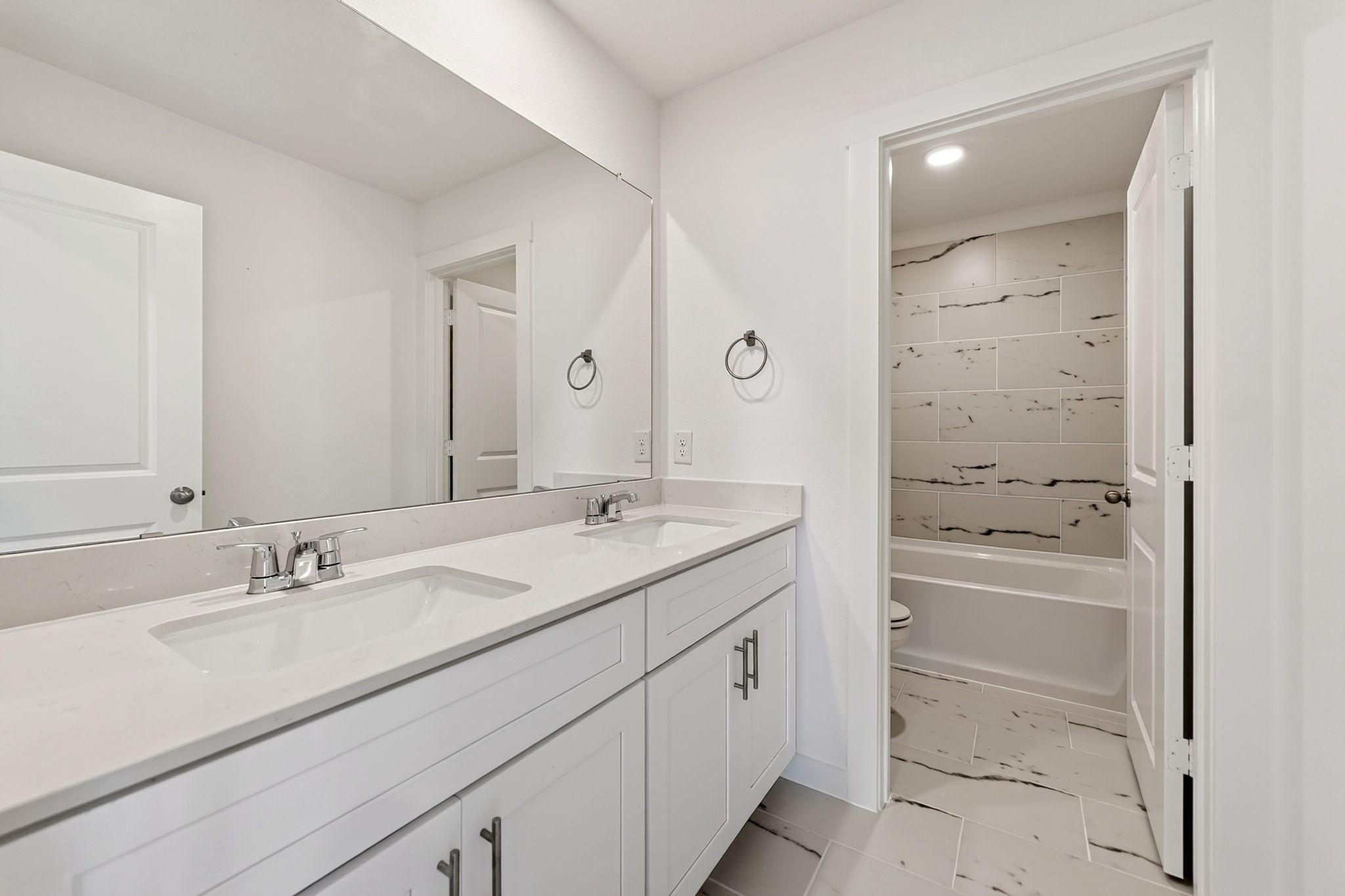 Double vanity bathroom with white cabinetry, marble tile shower, and soaking tub in Davidson Homes The Ash M, Josephine, Texas