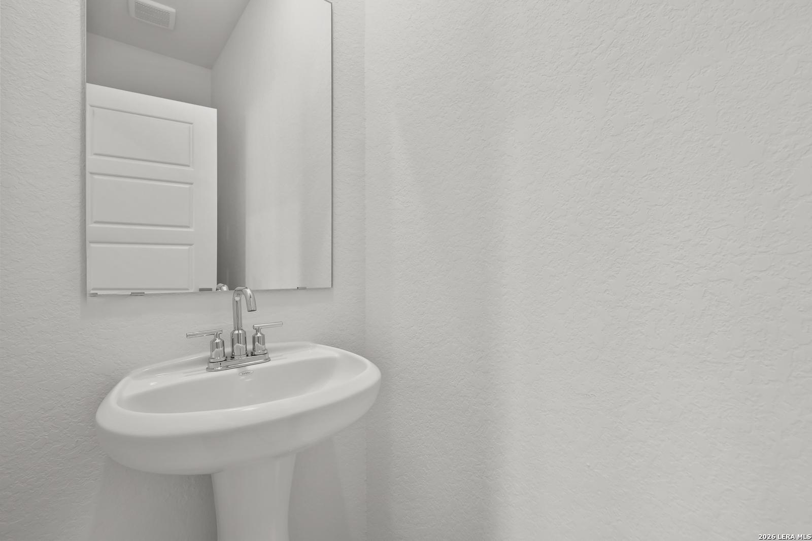 White pedestal sink with chrome faucet and mirrored vanity in powder room of Davidson Homes The Glenwood E, Elmendorf, Texas