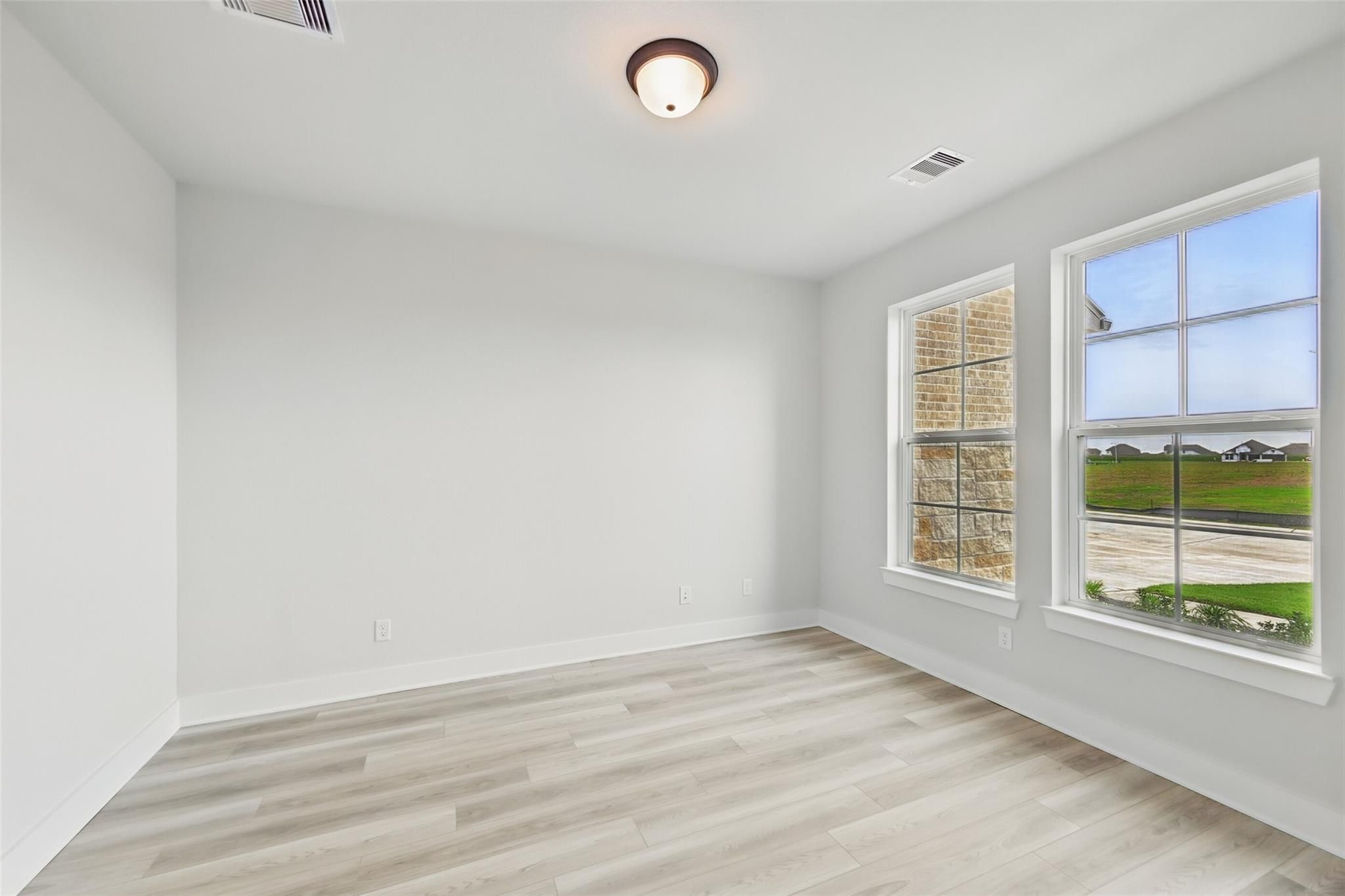 Spacious empty bedroom with light gray walls, laminate flooring, and large windows overlooking green fields in The Victoria C home, Lago Mar, Texas City