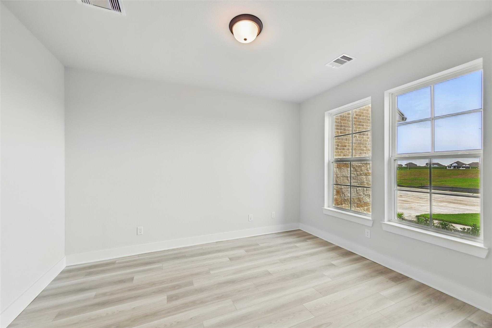 Bright empty bedroom with luxury vinyl plank flooring, large windows, and scenic green field views in Davidson Homes The Victoria C, Lago Mar, Texas City