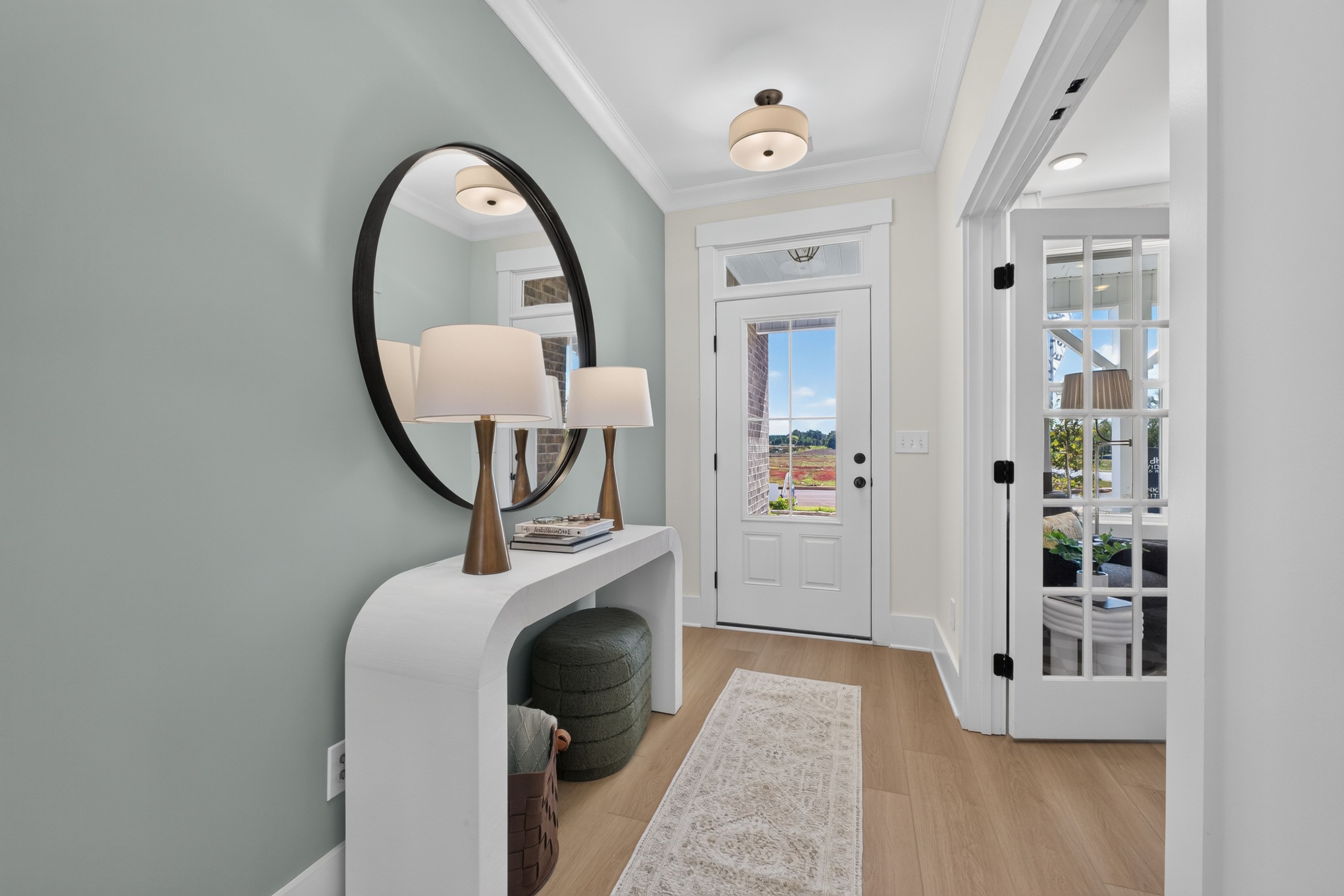 Bright foyer entry at Evergreen Mill in Madison, AL by Davidson Homes with round mirror, white console table, and glass-panel door