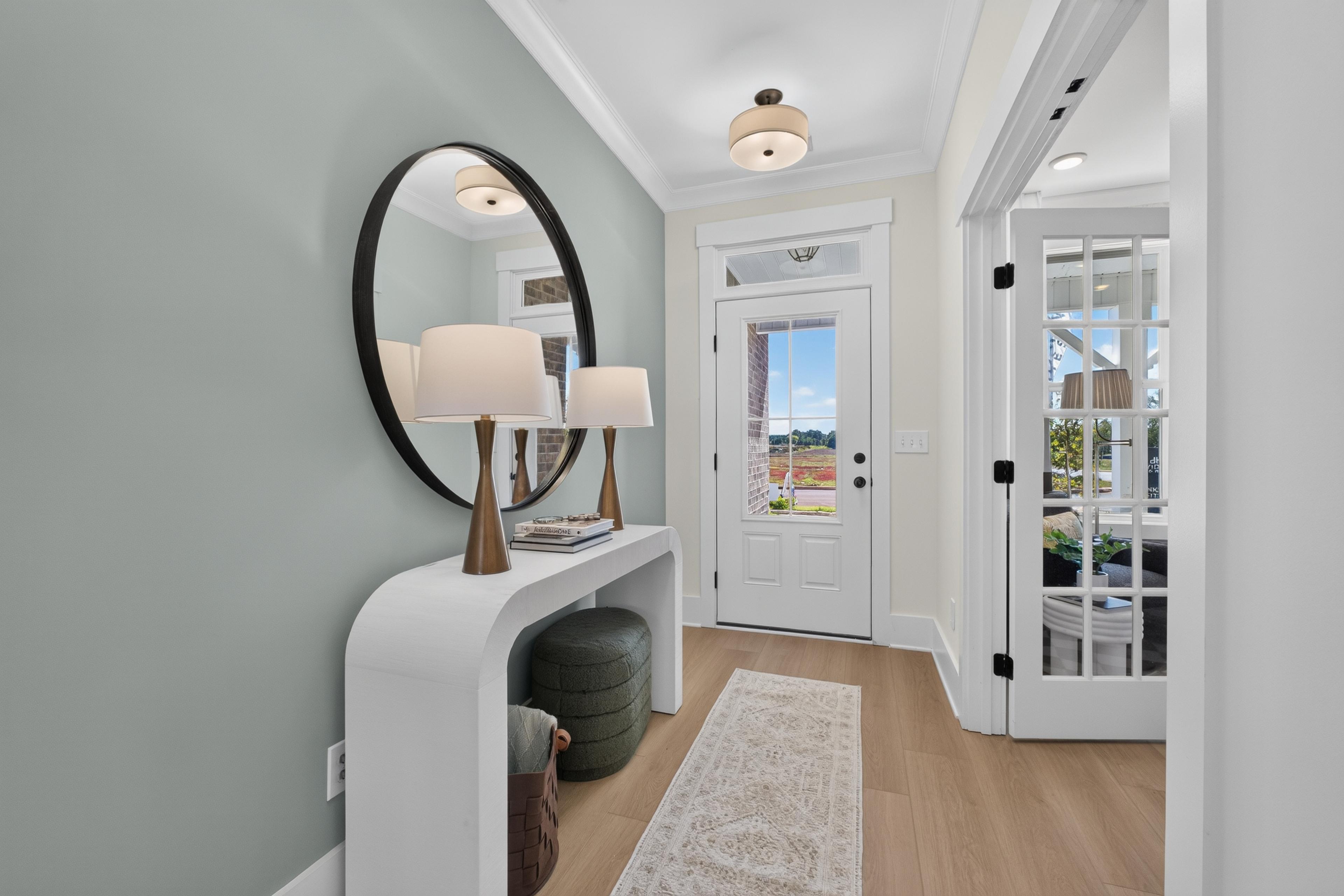 Bright foyer entry at Evergreen Mill in Madison, AL by Davidson Homes with round mirror, white console table, and glass-panel door