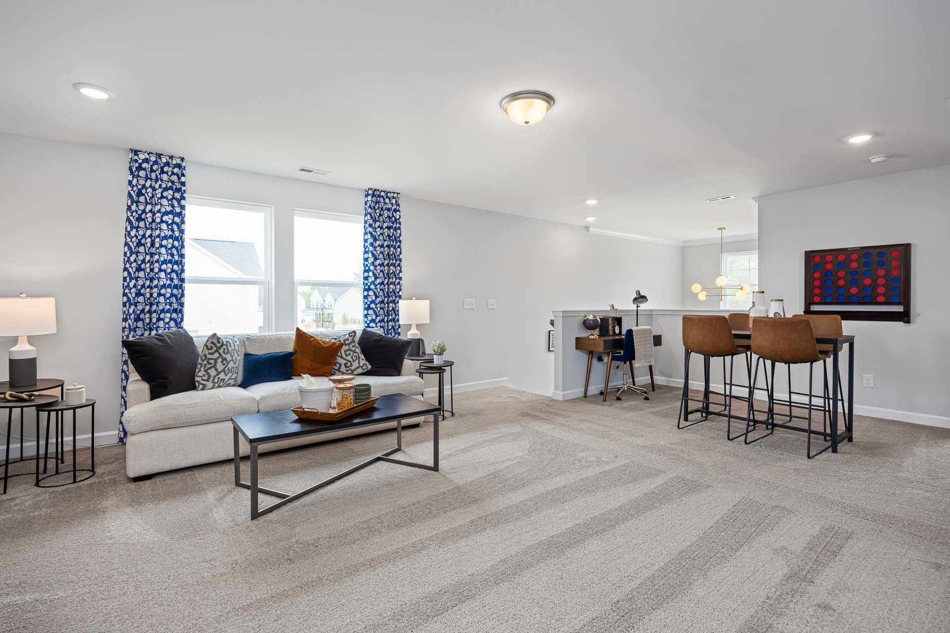 Spacious loft bonus room at Beverly Place in Four Oaks NC with gray walls, blue curtains, modern sofa, coffee table, and desk bar stools