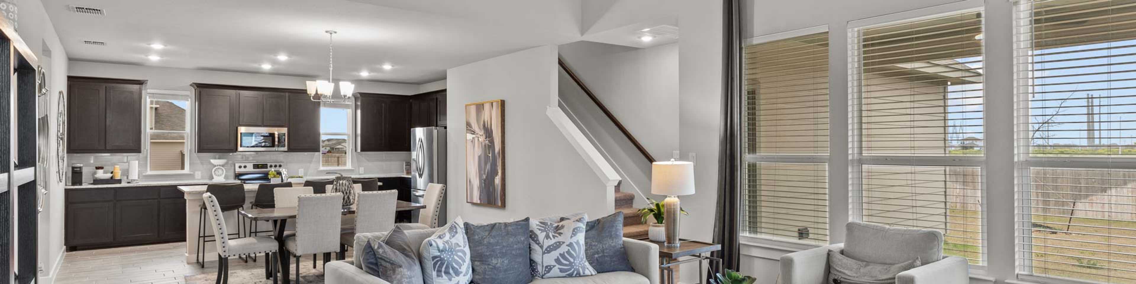 Modern open-concept living room with gray sofa, kitchen, and dining area in new Seguin home