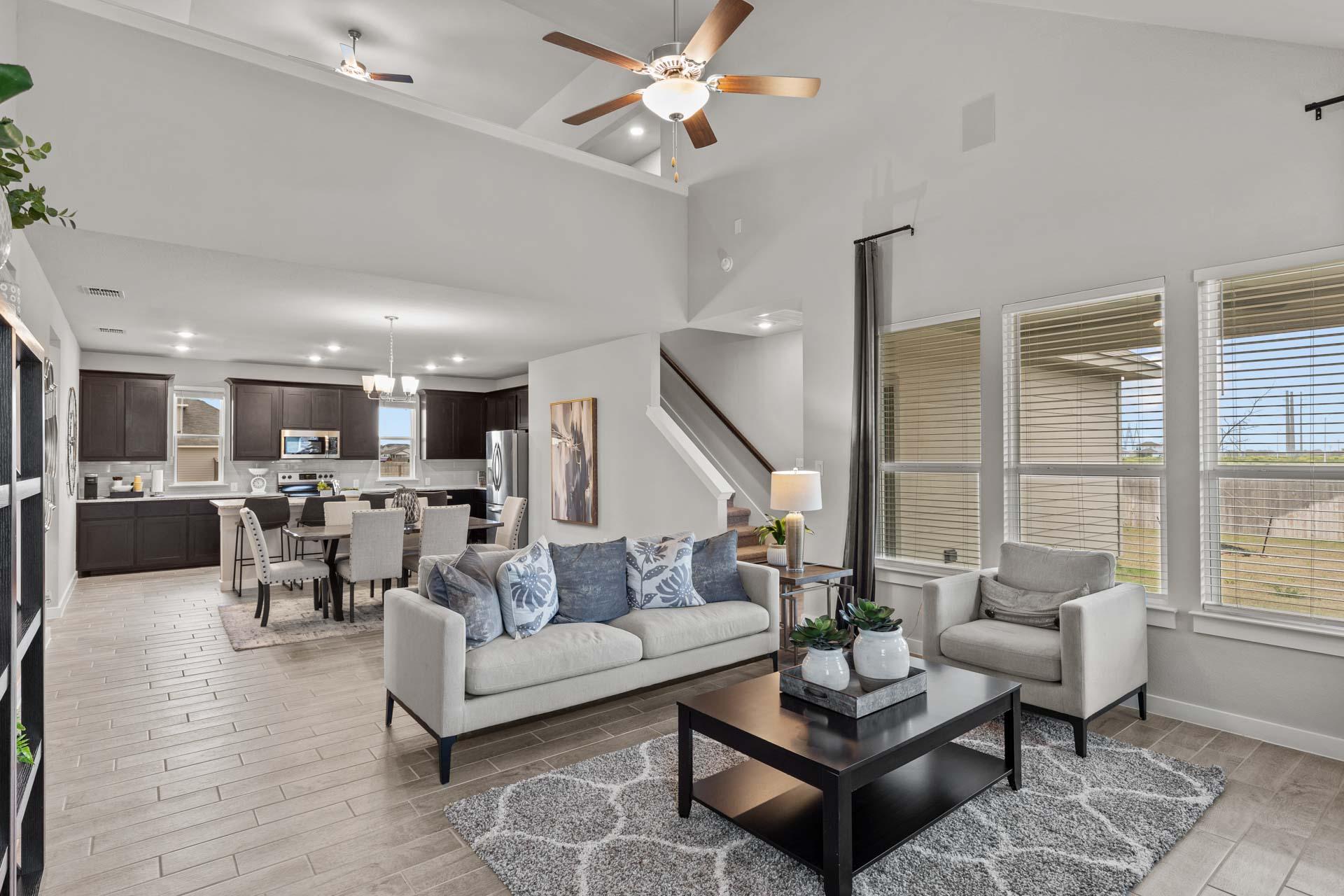 Spacious open-concept living room and kitchen in The Collin A by Davidson Homes, Seguin TX, with gray sofa, dark cabinets, ceiling fans