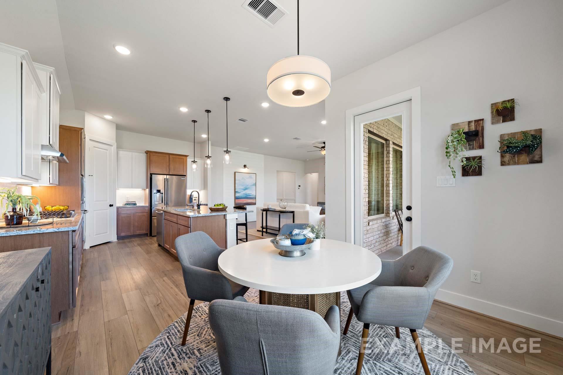 Open-concept kitchen and dining area with round table, gray chairs, wood floors, and glass doors to backyard in Davidson Homes The Edward A, Lago Mar, Texas