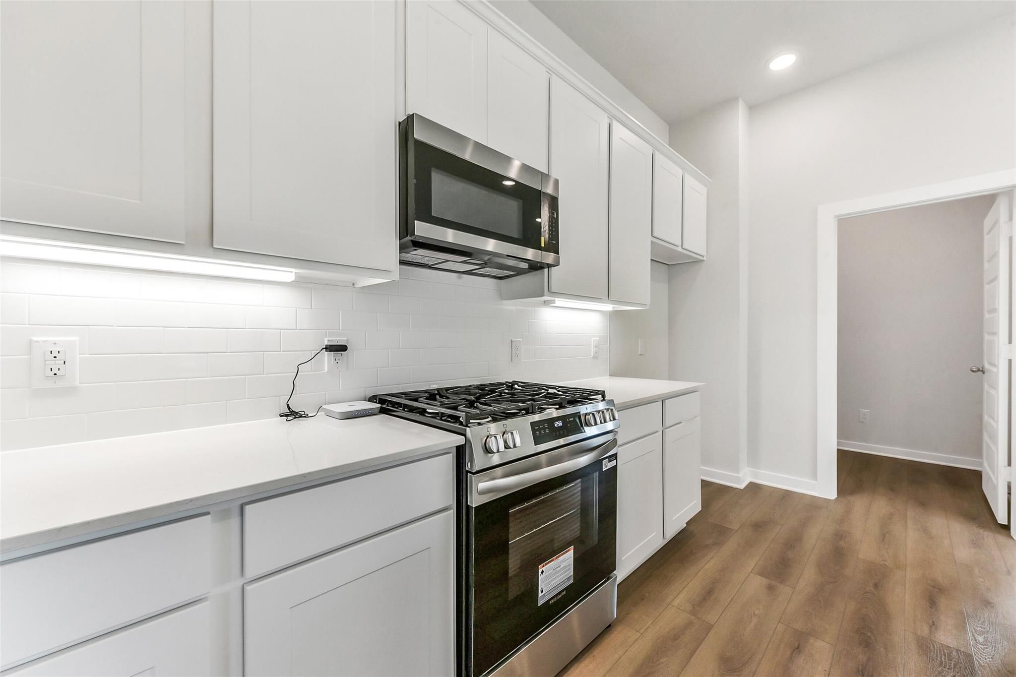 Bright modern kitchen with white cabinets, stainless steel appliances, gas cooktop in Davidson Homes The Costa B, Dayton, Texas