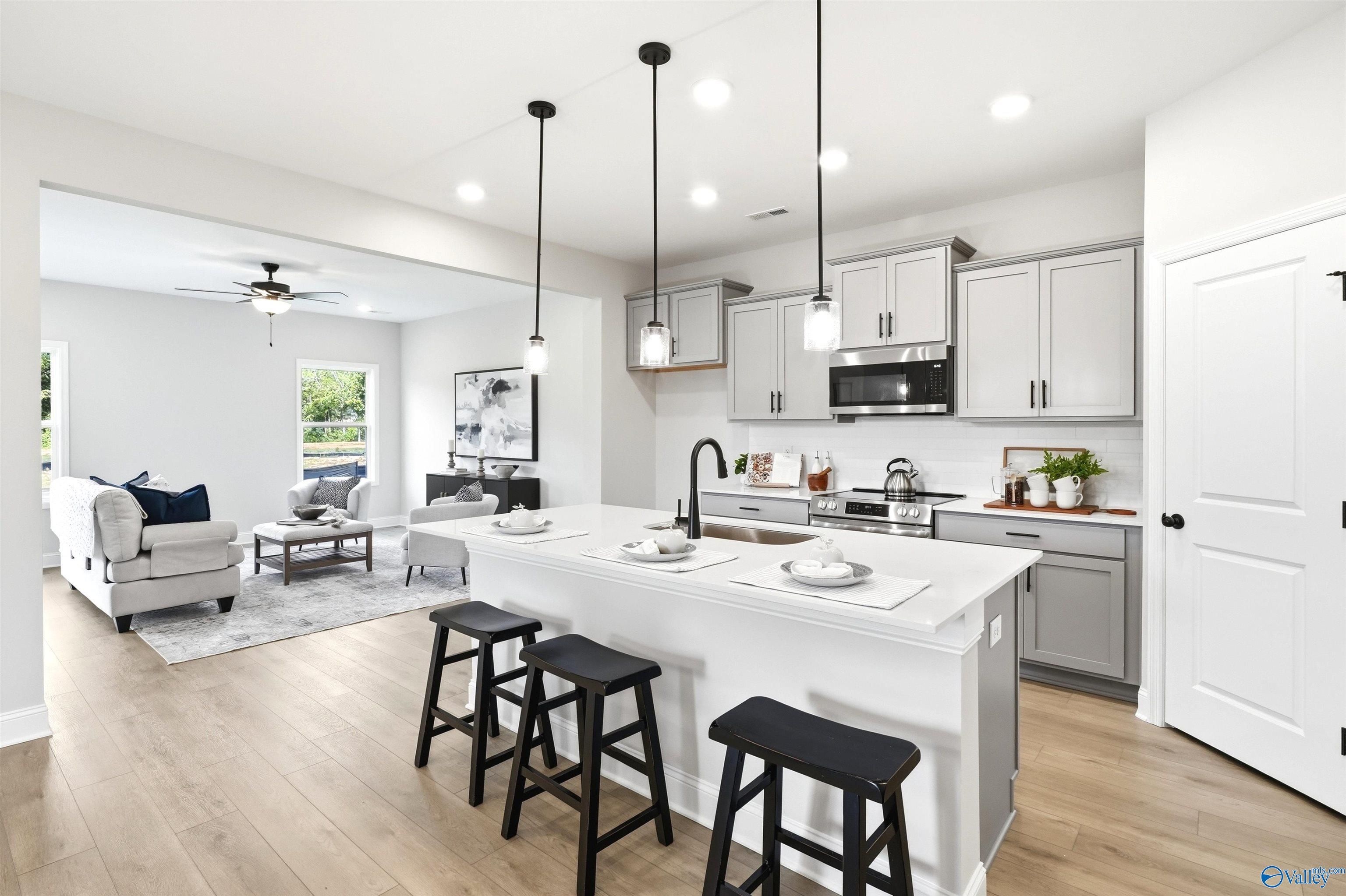 Kitchen island with black bar stools, gray cabinets, and open living room in Davidson Homes The Russell A, Huntsville, AL