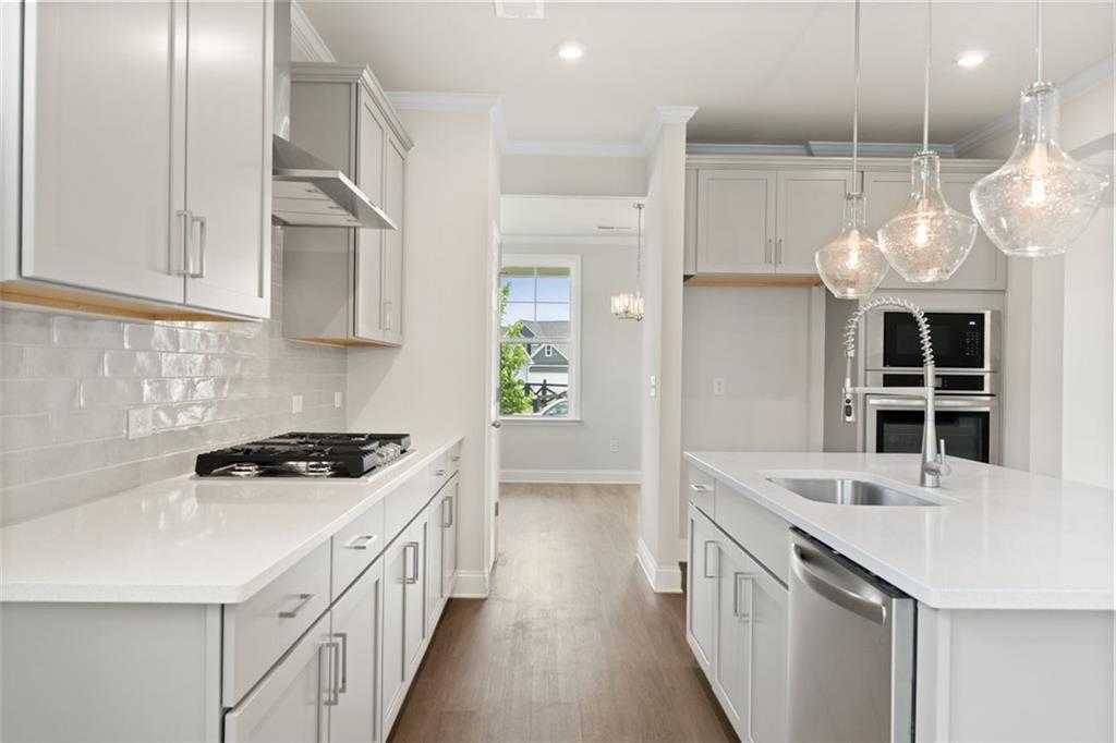 Modern white kitchen with quartz countertops, subway tile backsplash, stainless appliances, and pendant lights in The Willow D at Wehunt Meadows, Hoschton