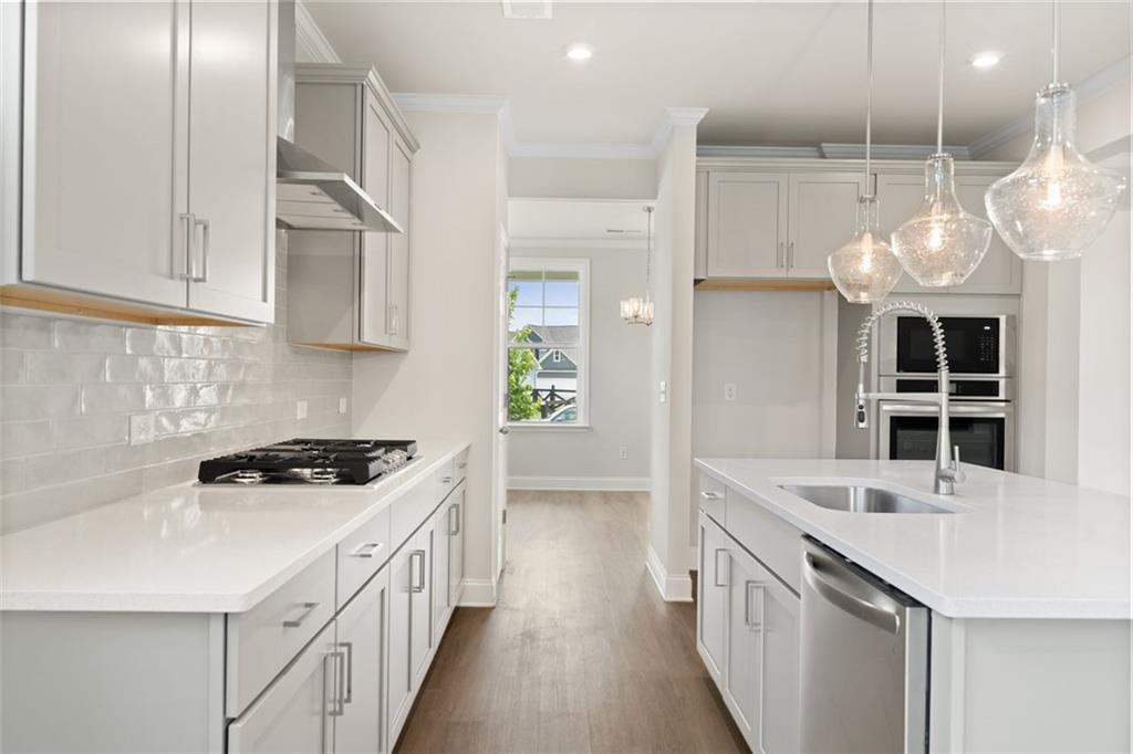 Modern white kitchen with quartz countertops, subway tile backsplash, stainless appliances, and pendant lights in The Willow D at Wehunt Meadows, Hoschton