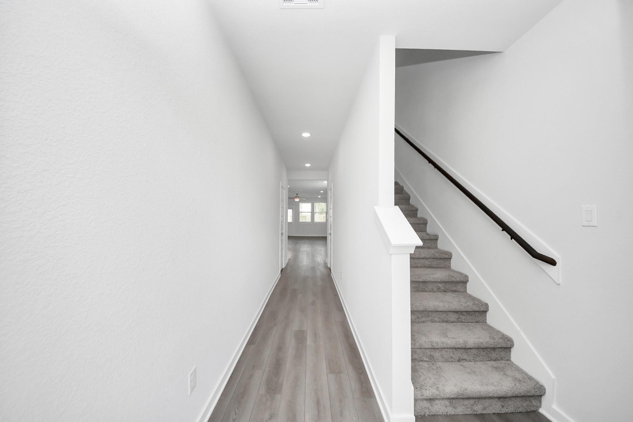 Bright hallway with wood-look flooring and carpeted staircase in The Brazos F floor plan at Liberty Estates, Cleveland, TX.