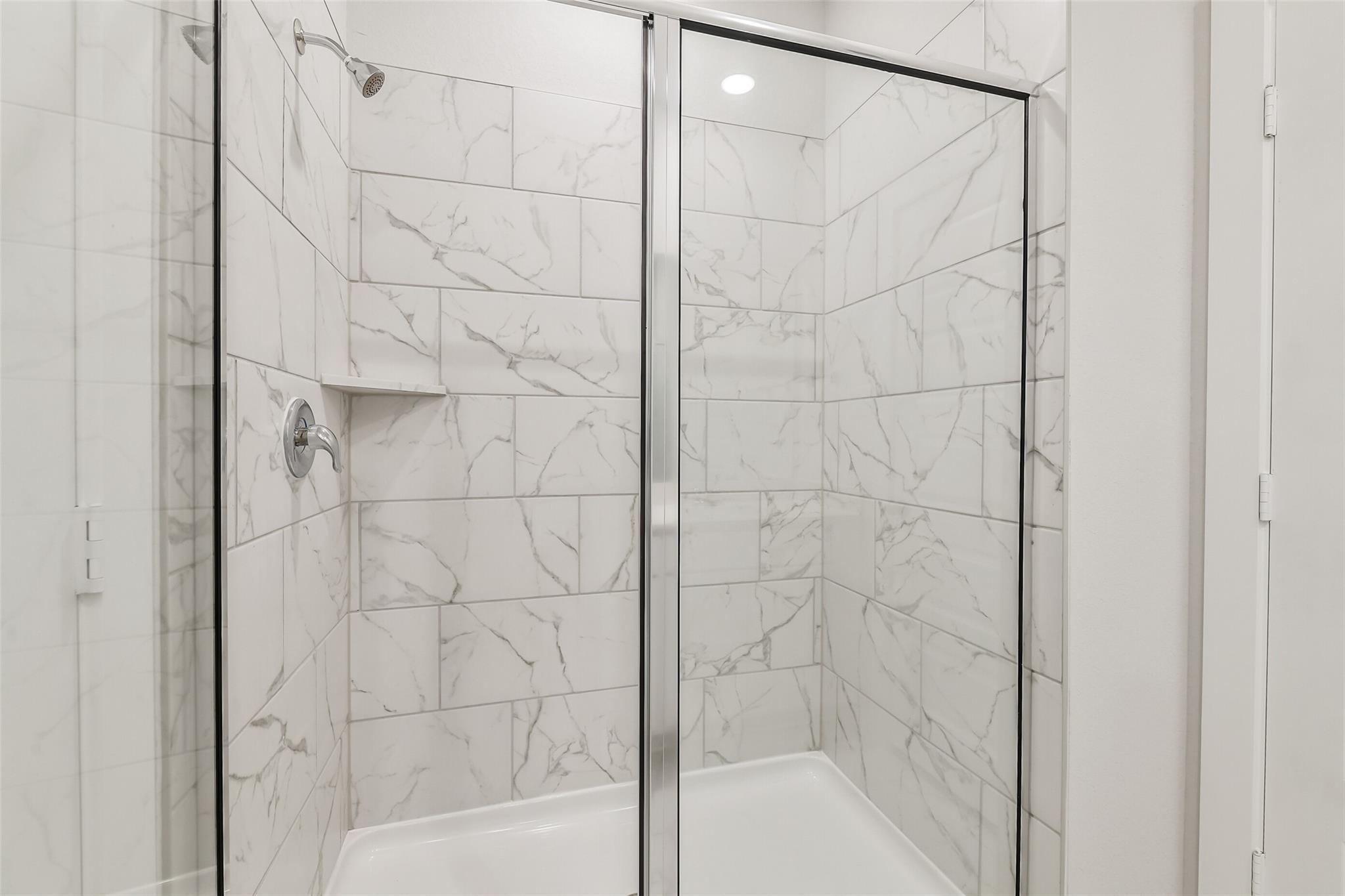 Elegant frameless glass walk-in shower with white marble tiles in master bath of Davidson Homes The San Marcos E, Conroe TX