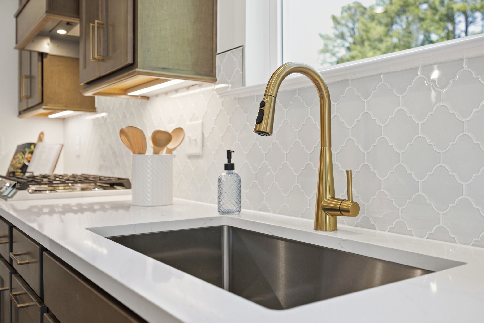 Modern kitchen sink area in The Ashport featuring gold faucet, quartz countertops, and elegant white tile backsplash.