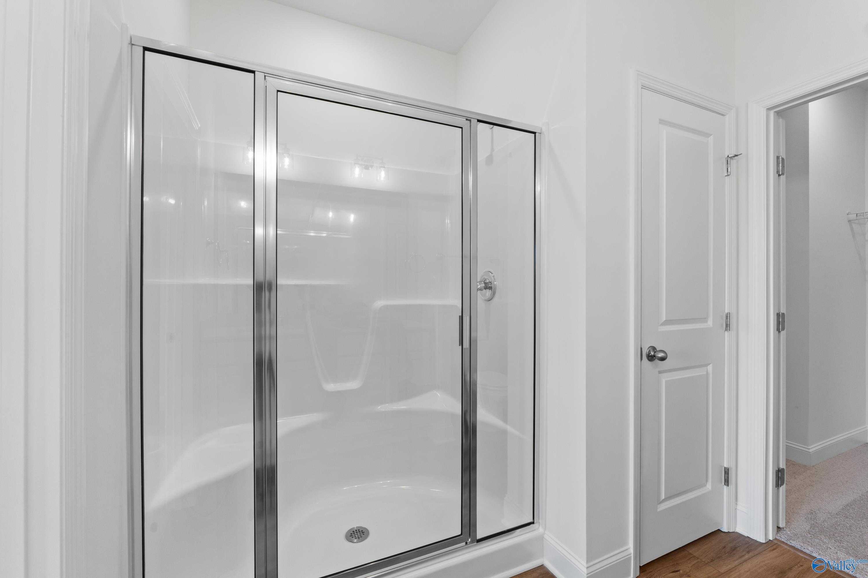 Elegant glass-enclosed shower-tub combo with white tiles and chrome fixtures in master bathroom of Davidson Homes The Asheville C in Hazel Green, Alabama
