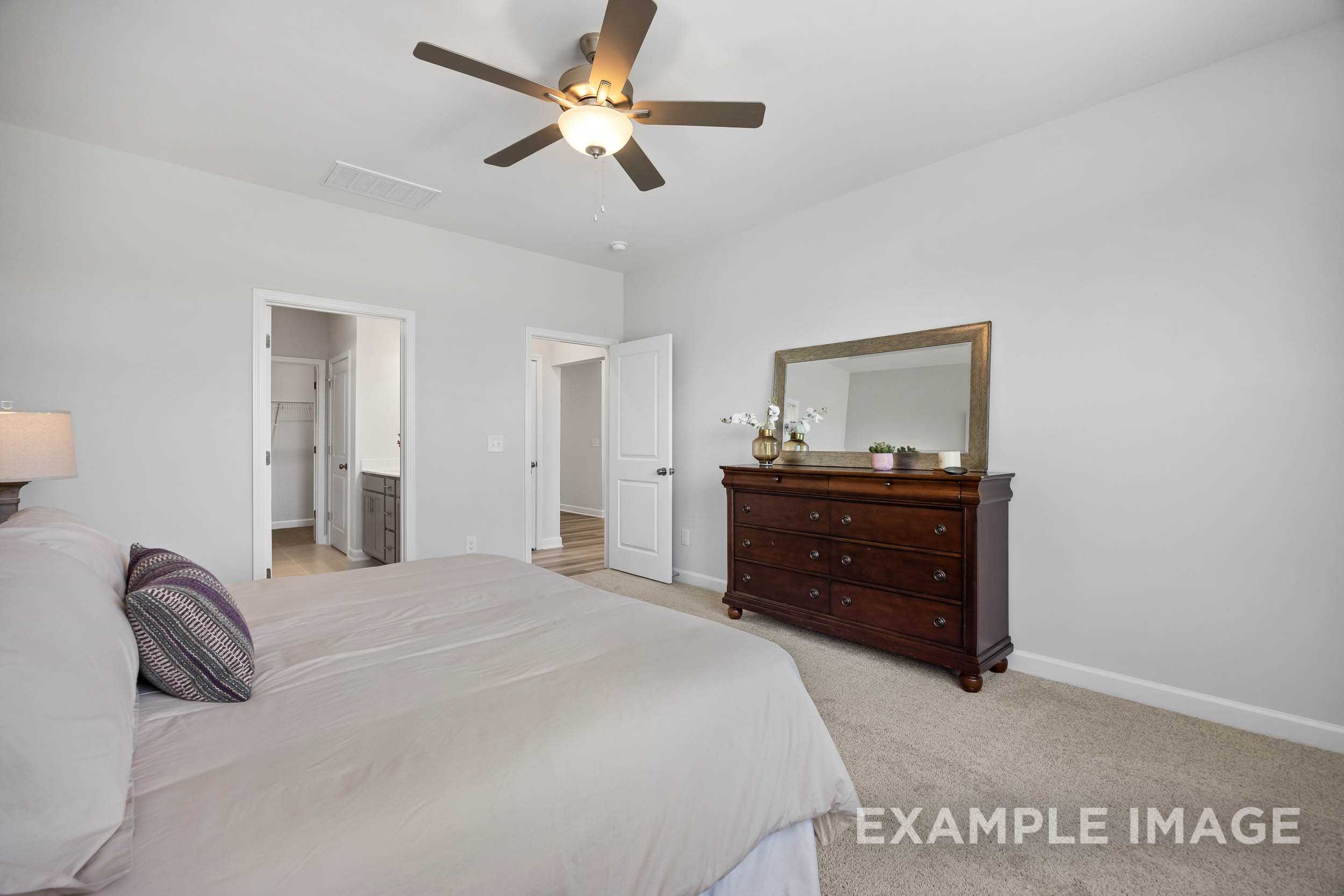 Spacious master bedroom in The Daphne C featuring king bed, wooden dresser with mirror, closet and bath doors, ceiling fan