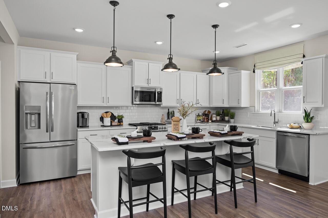 Modern white kitchen with stainless appliances, island bar stools, and pendant lights in Davidson Homes The Hickory II B, Zebulon, NC