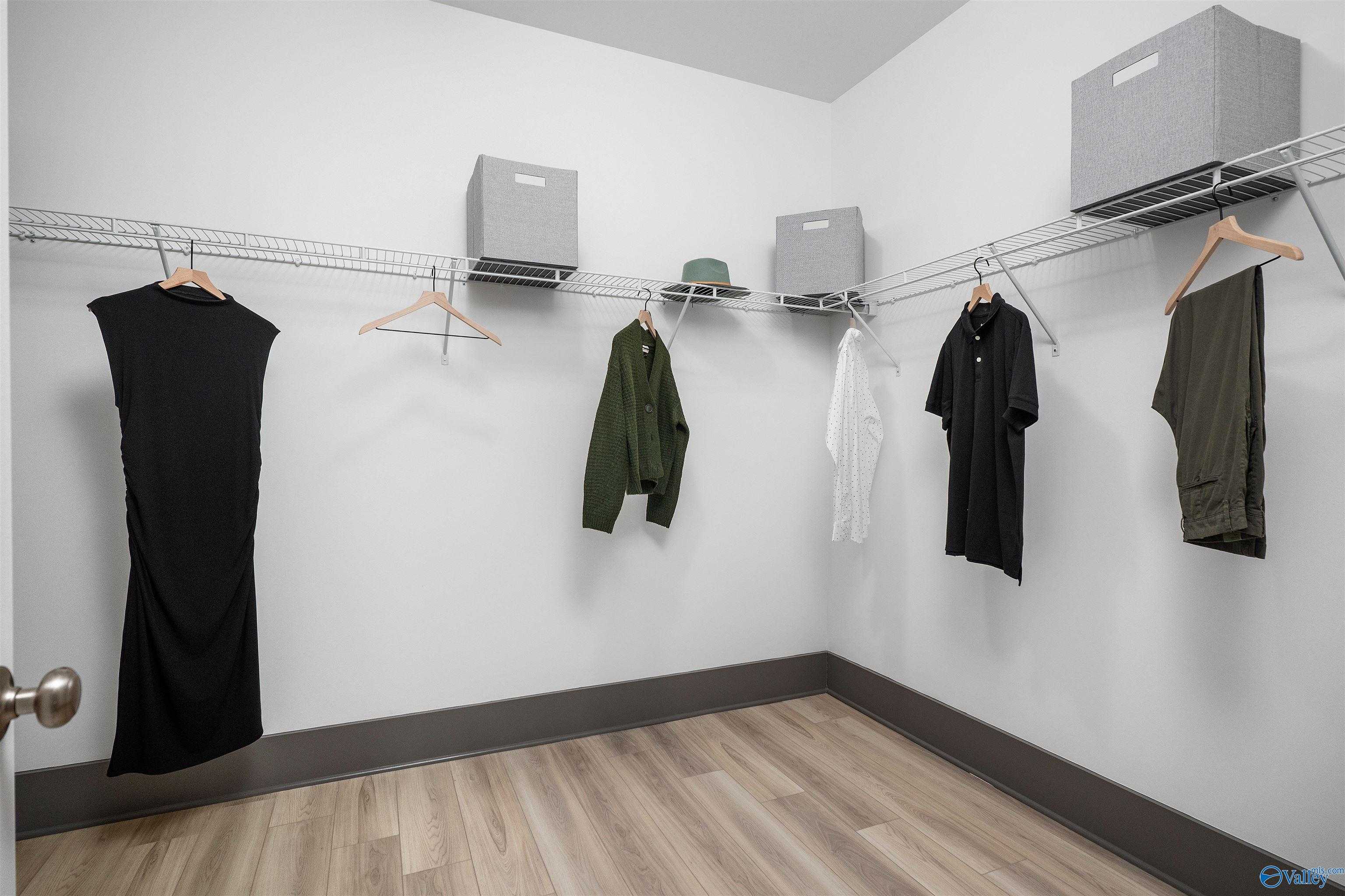 Organized walk-in closet with hanging dresses, jackets, shirts, pants, hat, and gray storage bins in Davidson Homes The Rockford B with Bonus, Madison, Alabama