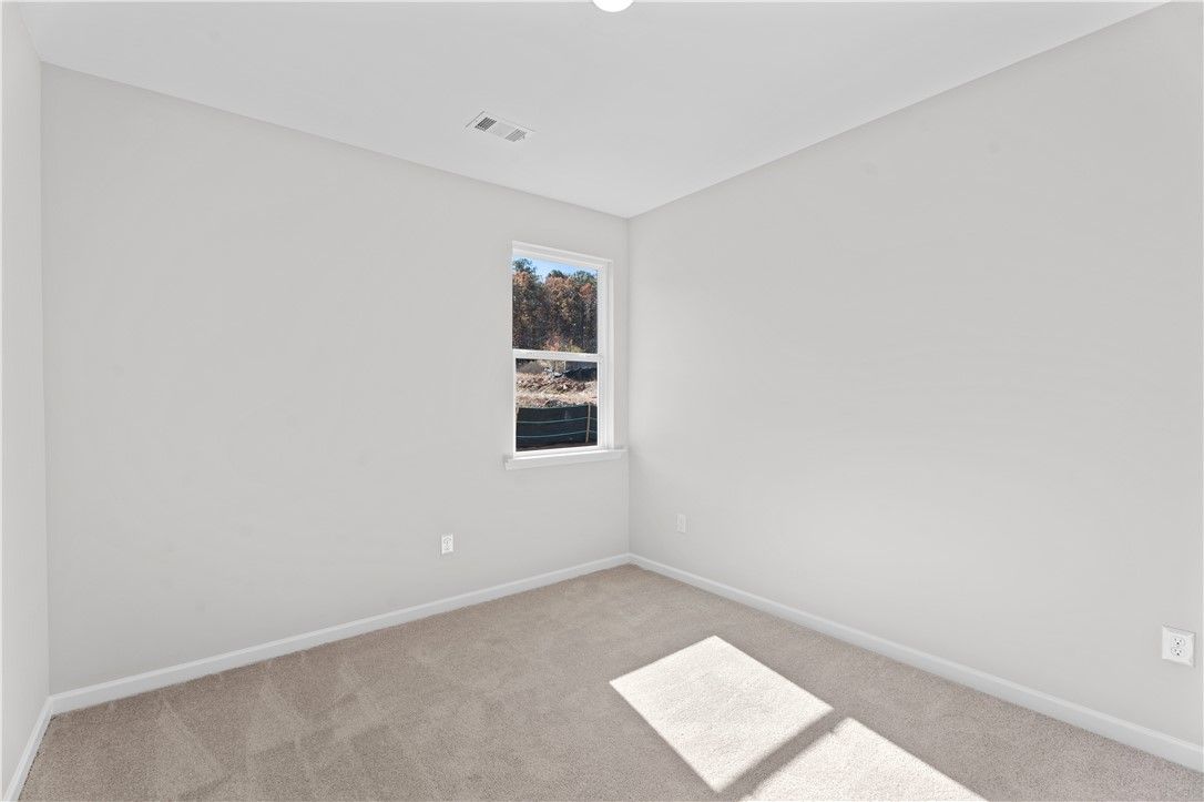Bright bedroom with neutral gray walls, carpet floor, and window view of trees in Davidson Homes The Luna B, Opelika, Alabama