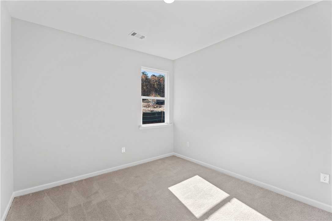 Bright bedroom with neutral gray walls, carpet floor, and window view of trees in Davidson Homes The Luna B, Opelika, Alabama