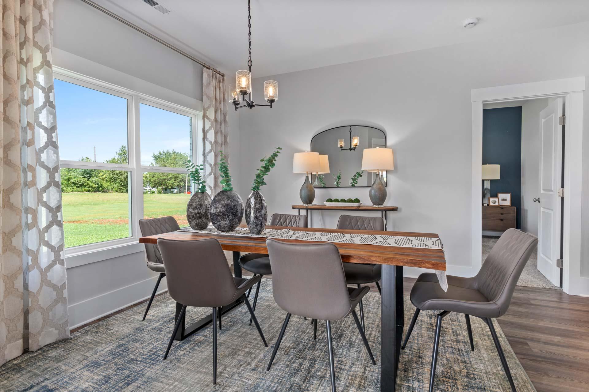 Elegant dining room in Blue Spring, Huntsville AL with live-edge wood table, gray upholstered chairs, chandelier and lush window views