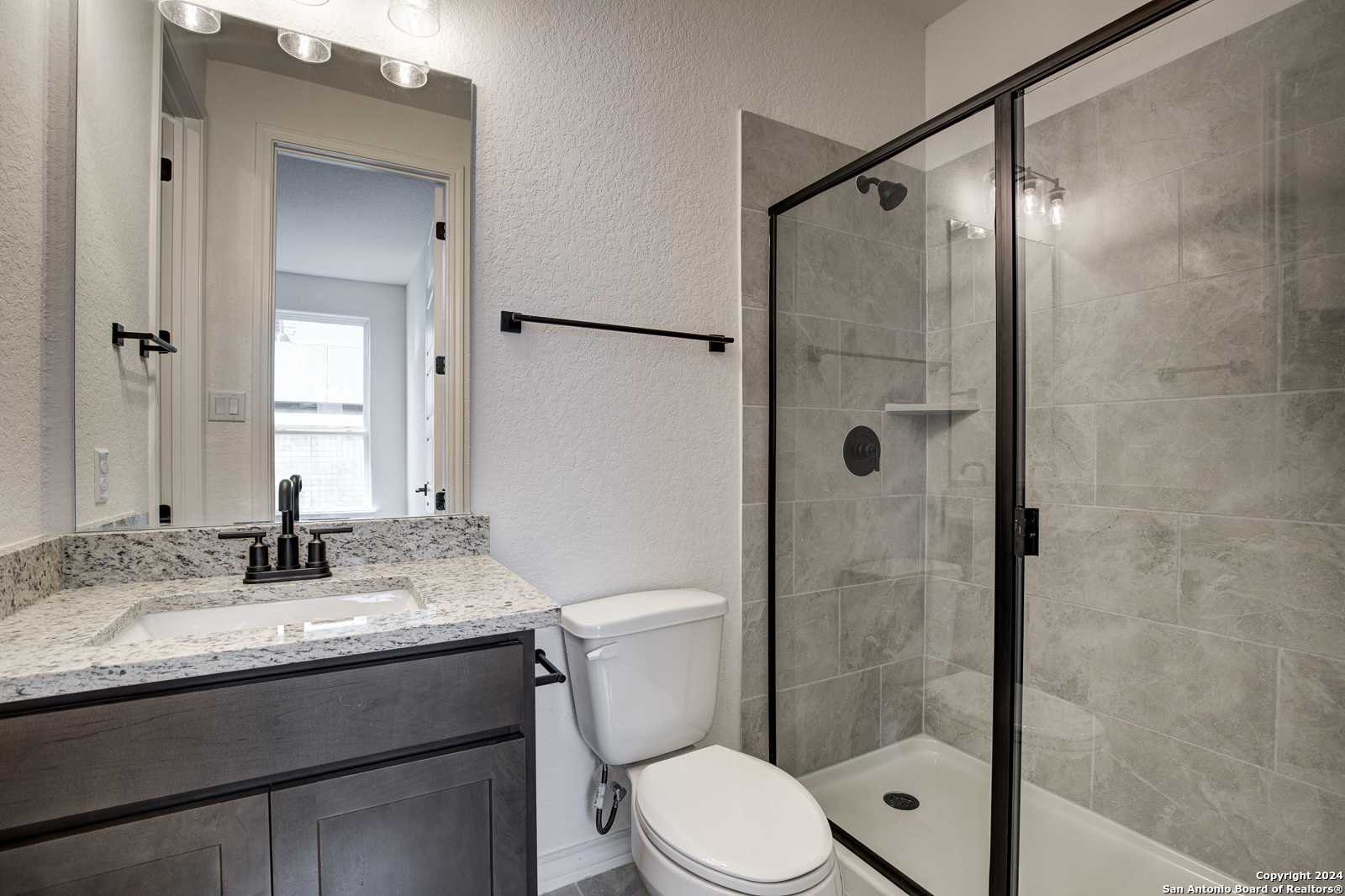 Modern master bathroom with frameless glass shower, quartz vanity, round mirror in Davidson Homes The Garner B, Castroville, TX