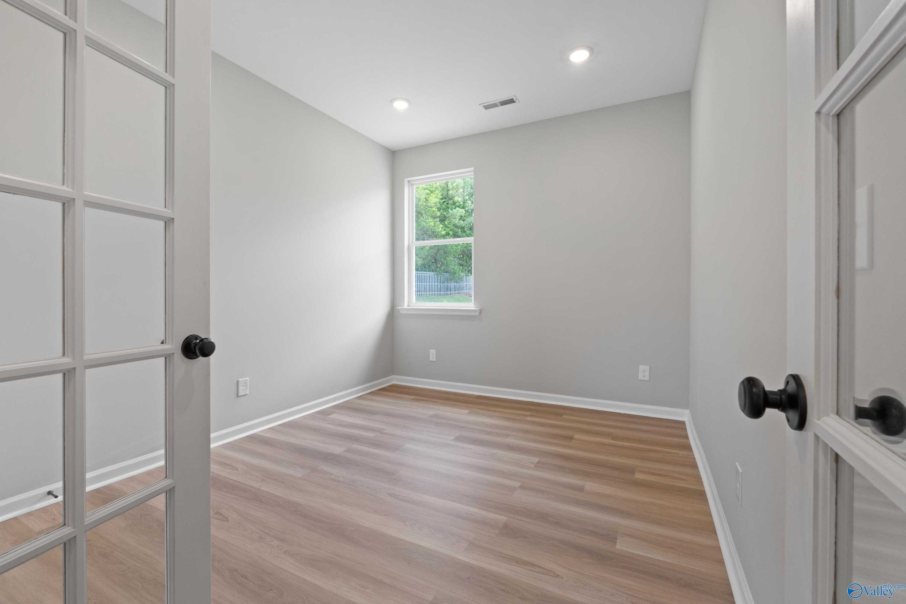 Bright secondary bedroom with light gray walls, hardwood floors, and large window in The Nantucket by Evermore Homes, Madison AL