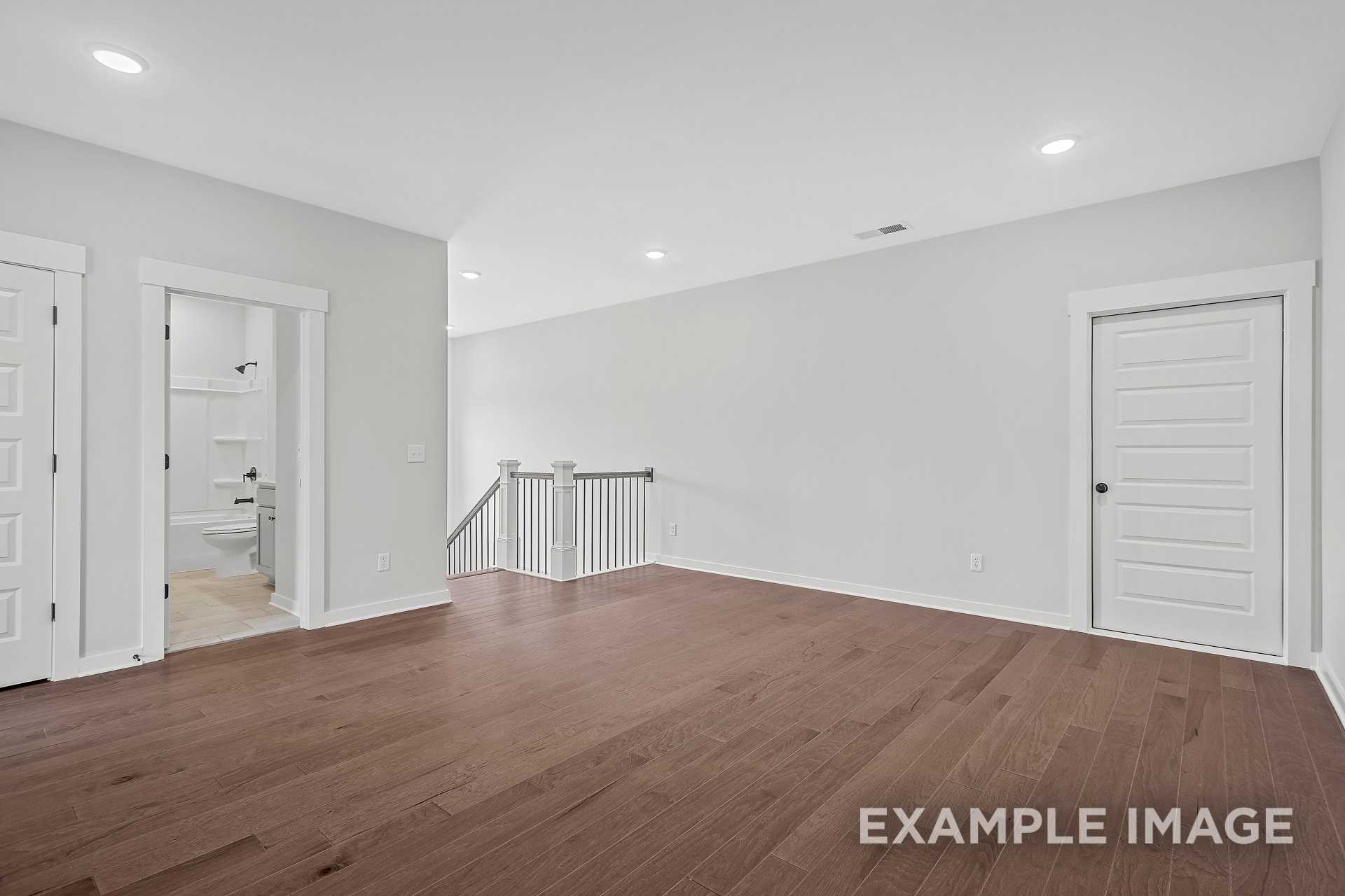 Spacious upstairs hallway in The Hathaway with hardwood floors, white doors, bathroom access, and open staircase railing