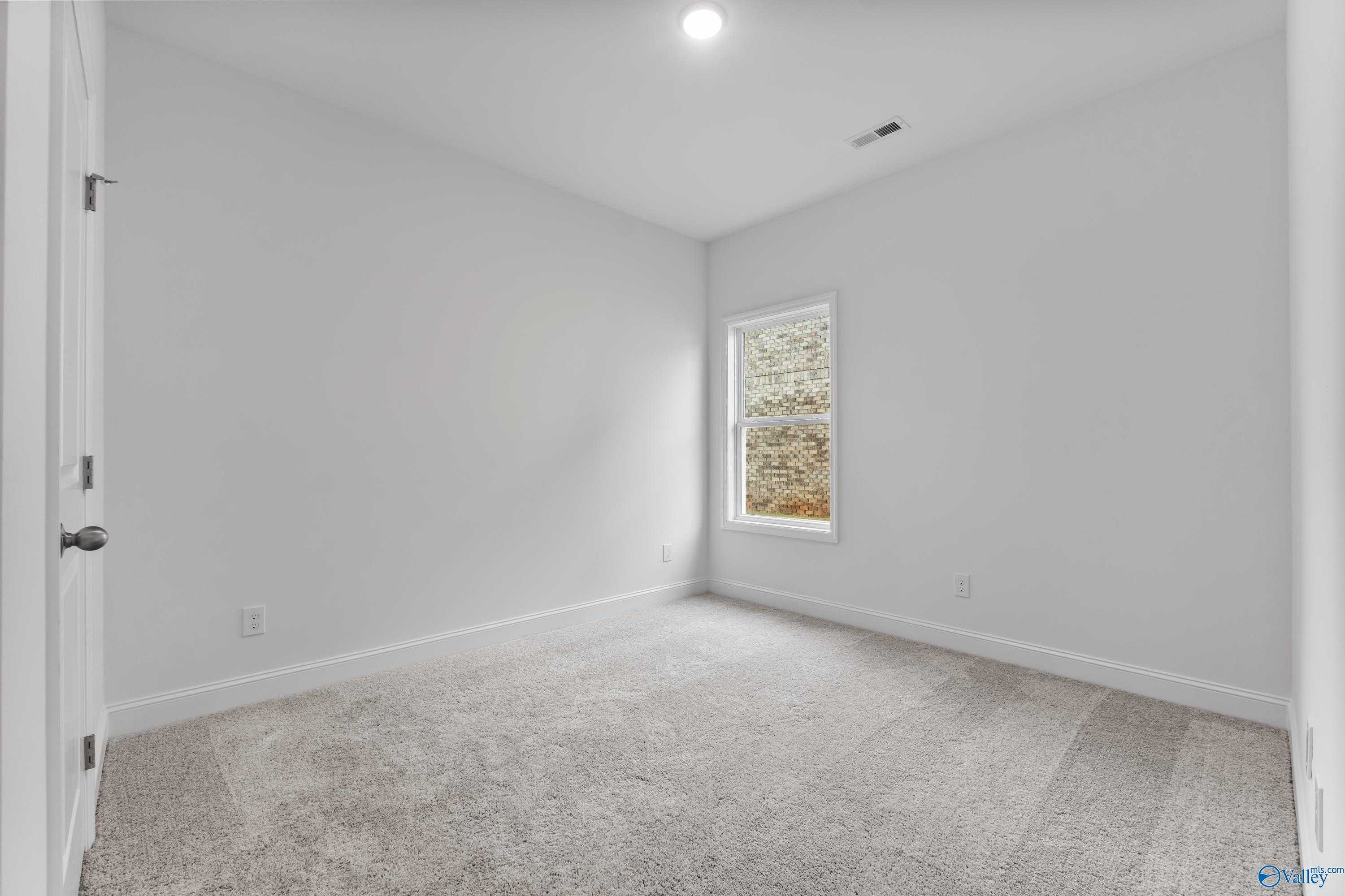 Empty bedroom with white walls, carpet flooring, large window, and open door in Davidson Homes The Asheville C, New Market, Alabama