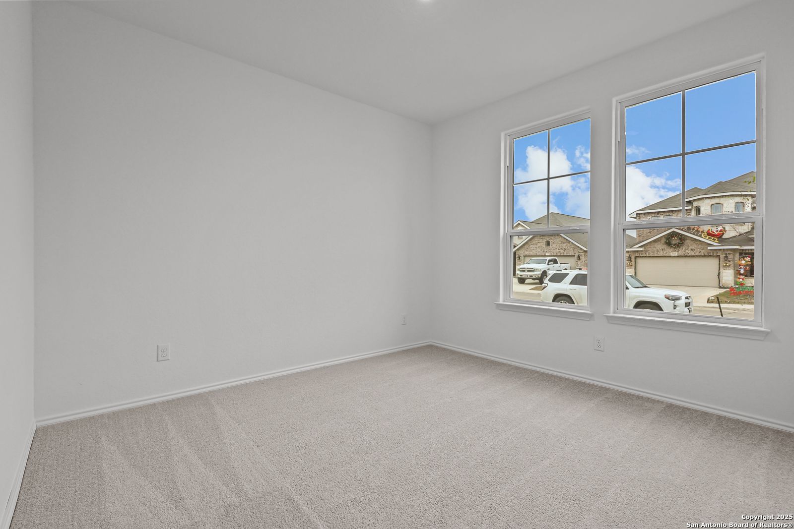 Bright empty bedroom with white walls, carpet floor, and large windows showing suburban neighborhood in Davidson Homes The Daphne J, Converse, Texas