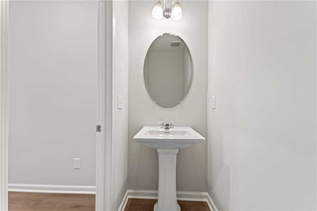 Elegant powder room featuring pedestal sink and oval mirror in Davidson Homes The Monroe A, Stegall Village, Emerson, Georgia