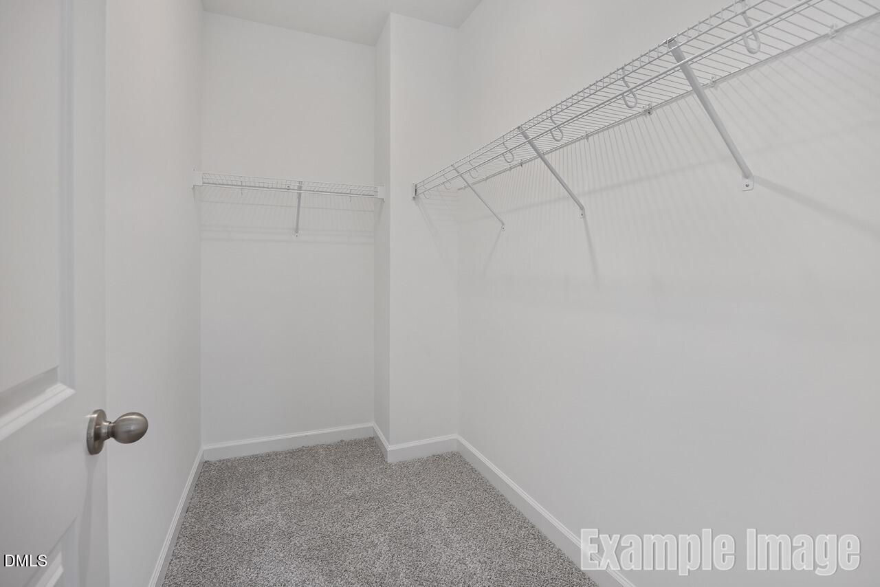 Spacious walk-in closet with wire shelving and gray carpet in master suite of Davidson Homes The Carter C, Gregory Village, Lillington, NC