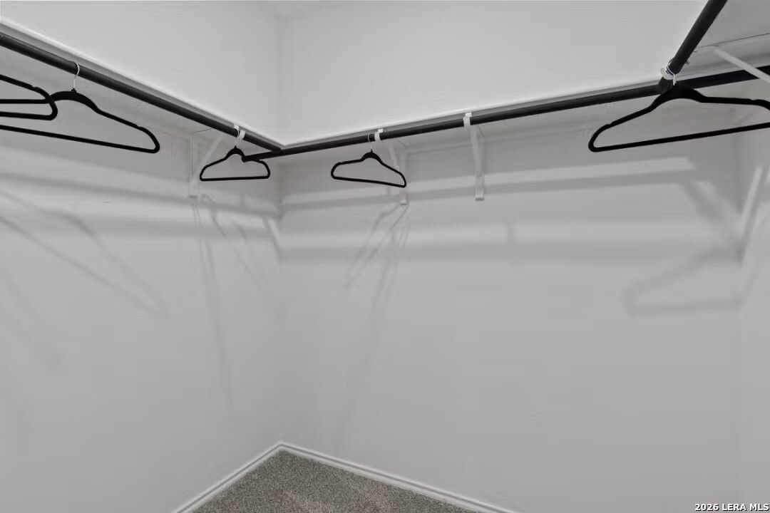 Spacious corner walk-in closet with double hanging rods and empty hangers in Davidson Homes The Douglas C, Converse Texas