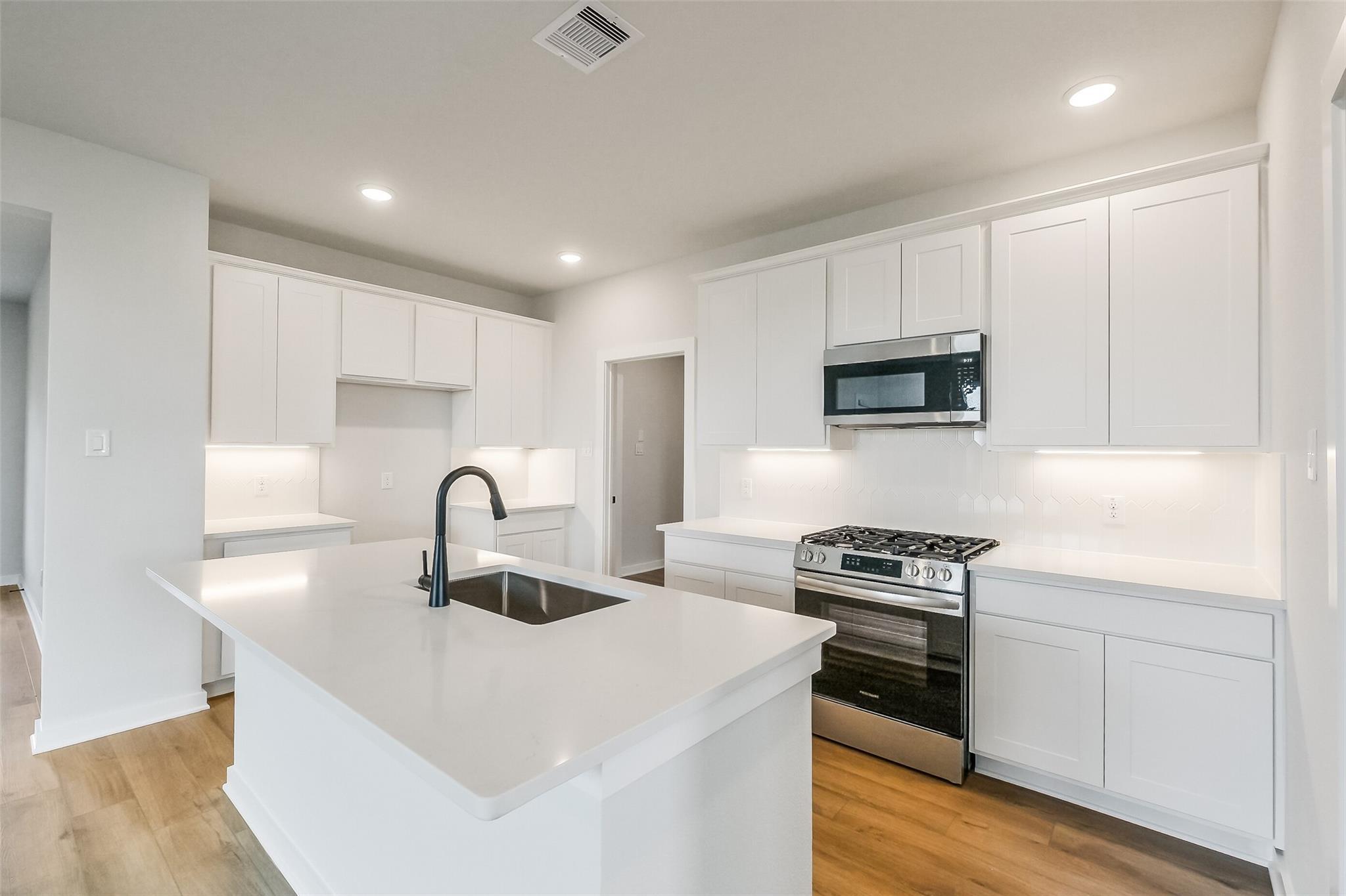 Modern white kitchen with quartz island, stainless gas range in Davidson Homes The Tierra B, Beasley, Texas