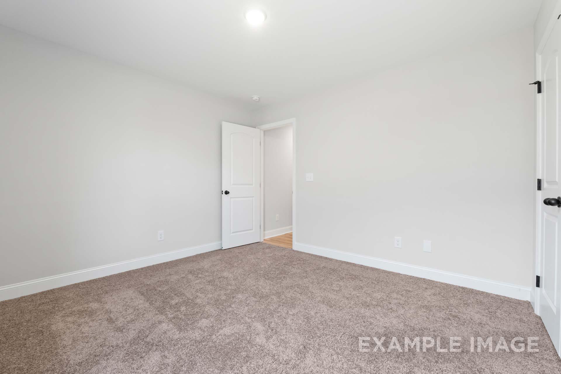 Spacious secondary bedroom in The Holly M with neutral gray walls, beige carpet, and doors to closet and bath