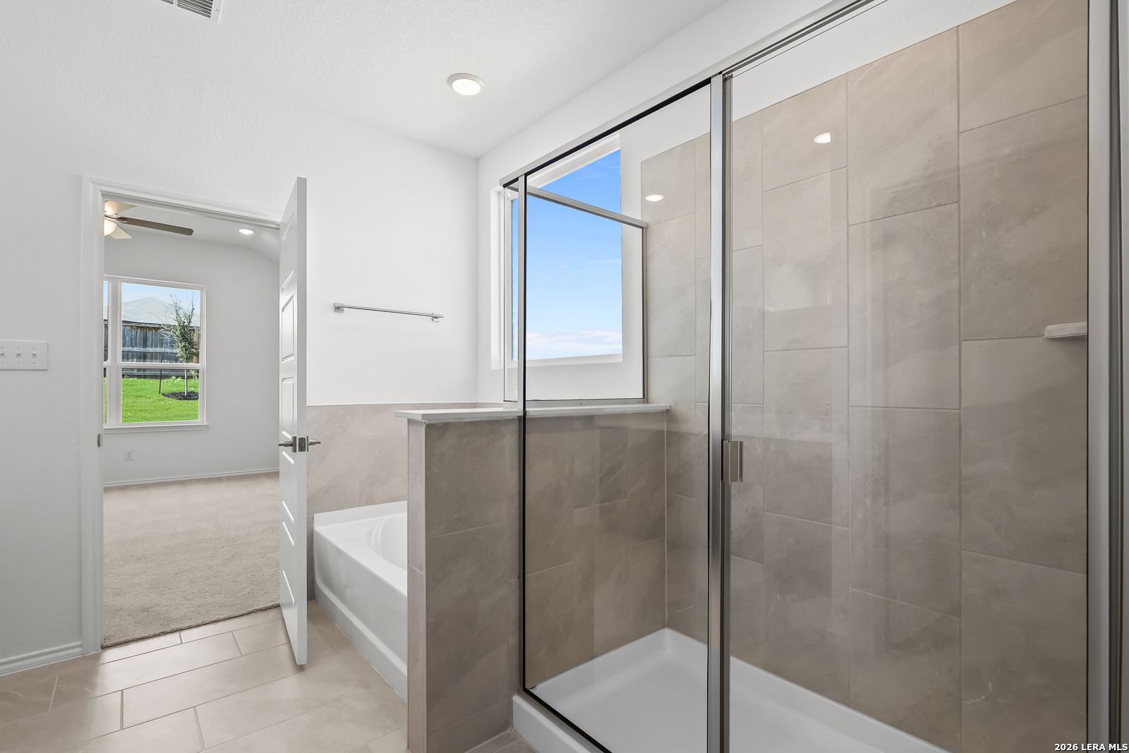 Luxurious master bathroom with soaking tub, frameless glass shower, and beige tile in Davidson Homes Sequoia B, San Antonio