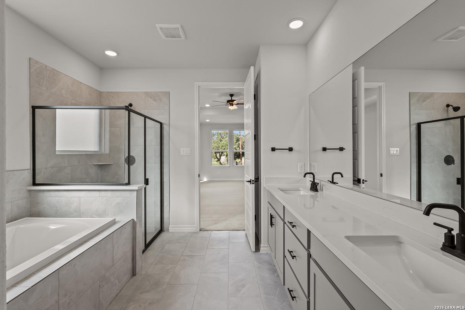 Modern master bathroom with soaking tub, glass shower, dual vanities and matte black fixtures in Davidson Homes' Oxford F plan, Castroville TX