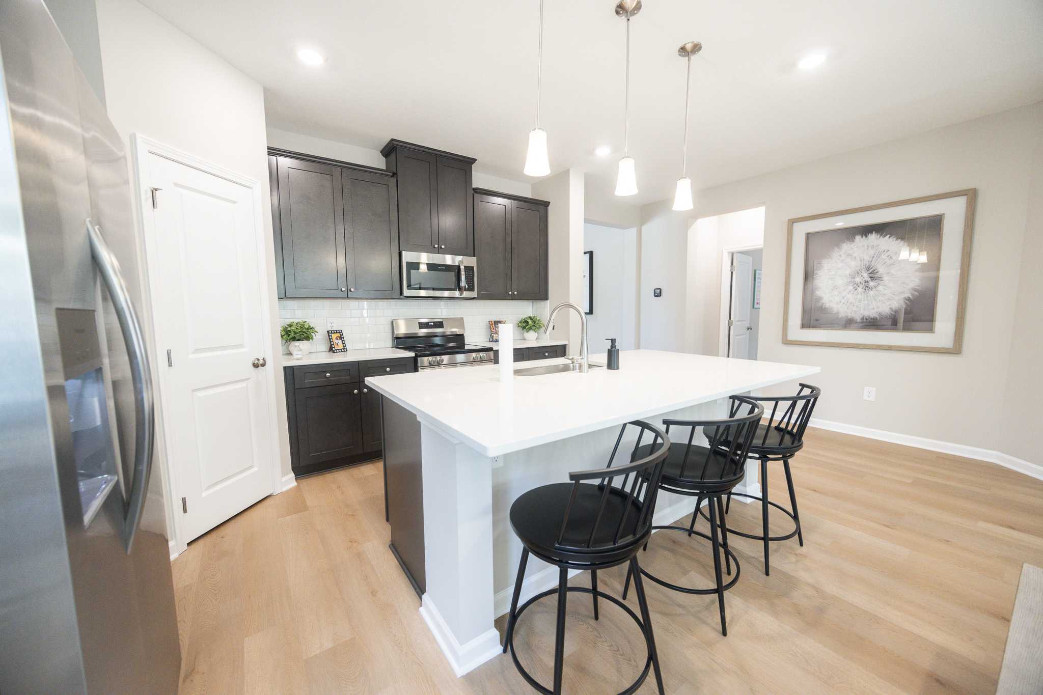 Spacious modern kitchen with dark cabinets, white island, black stools, stainless appliances, and hardwood floors at Silver Oak, Cusseta AL