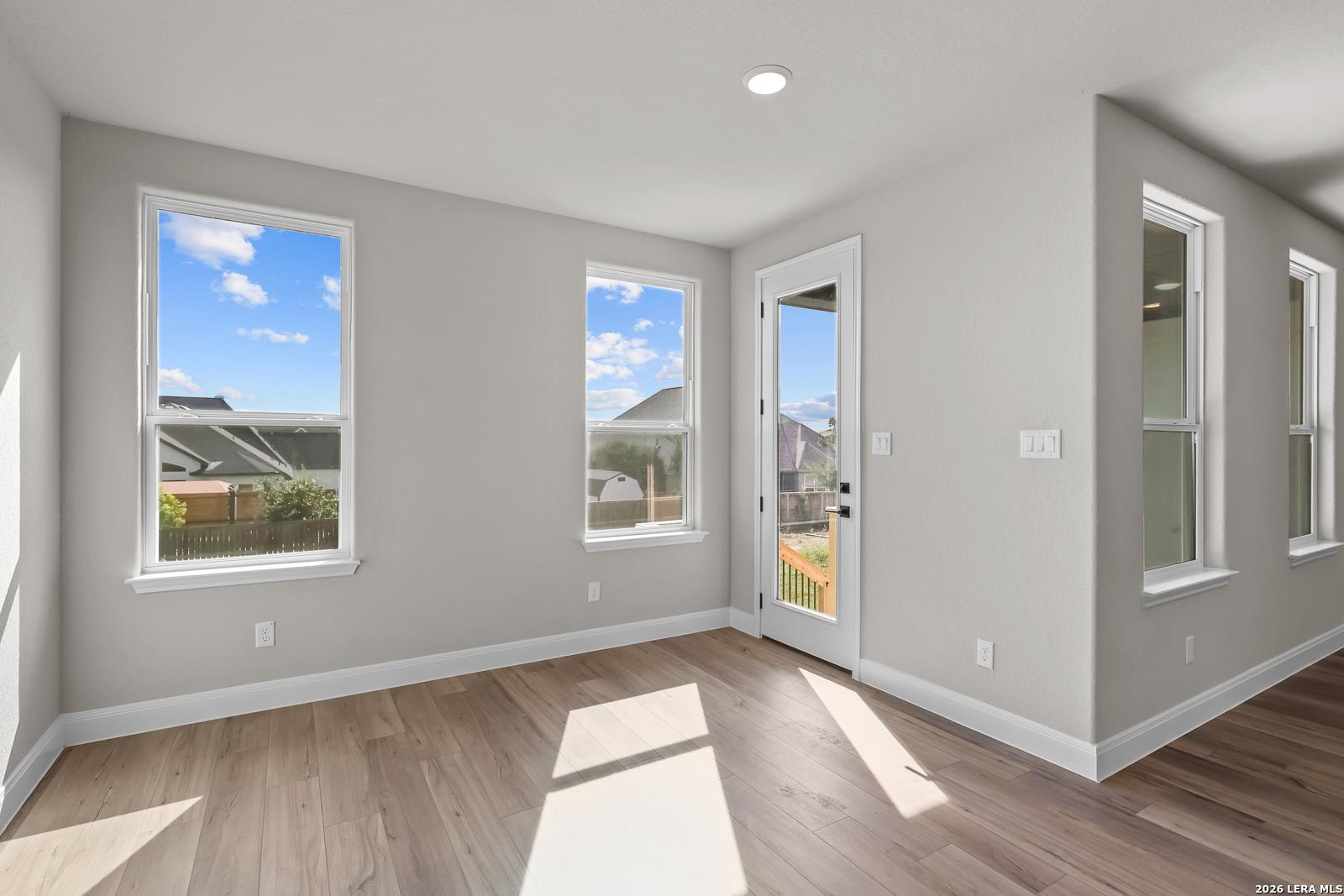 Bright room with wood-look flooring, windows, and glass back door to patio in Davidson Homes The Foster E, Potranco Oaks, Castroville TX